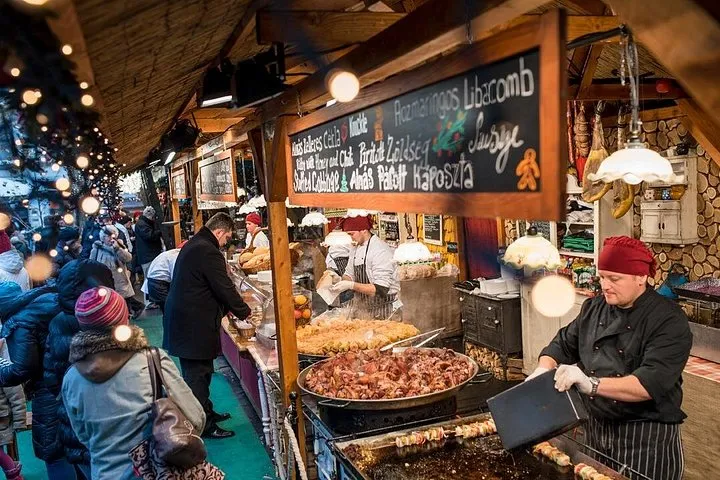 A guide and a small group at a lit-up stall on a Budapest Christmas market tour with chimney cake and mulled wine