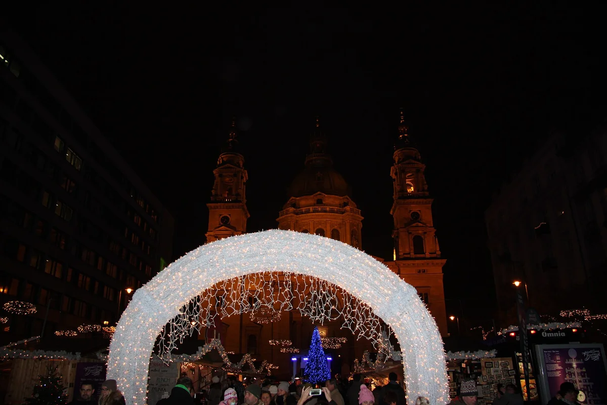 The lit arch over the Christmas market in front of St Stephen's Basilica at night, a stop on most Budapest Christmas market tours