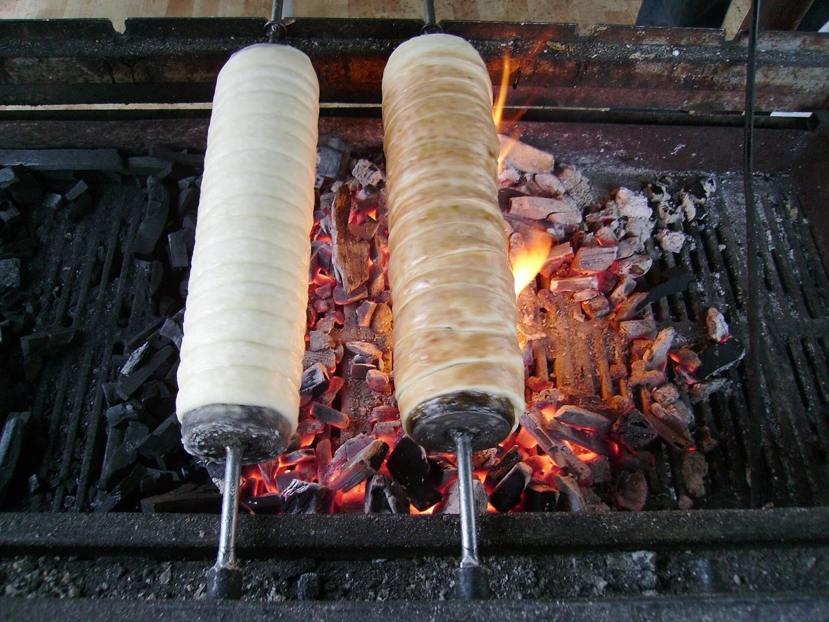 Two chimney cakes roasting over charcoal, the treat on a Budapest Christmas markets tour with chimney cake